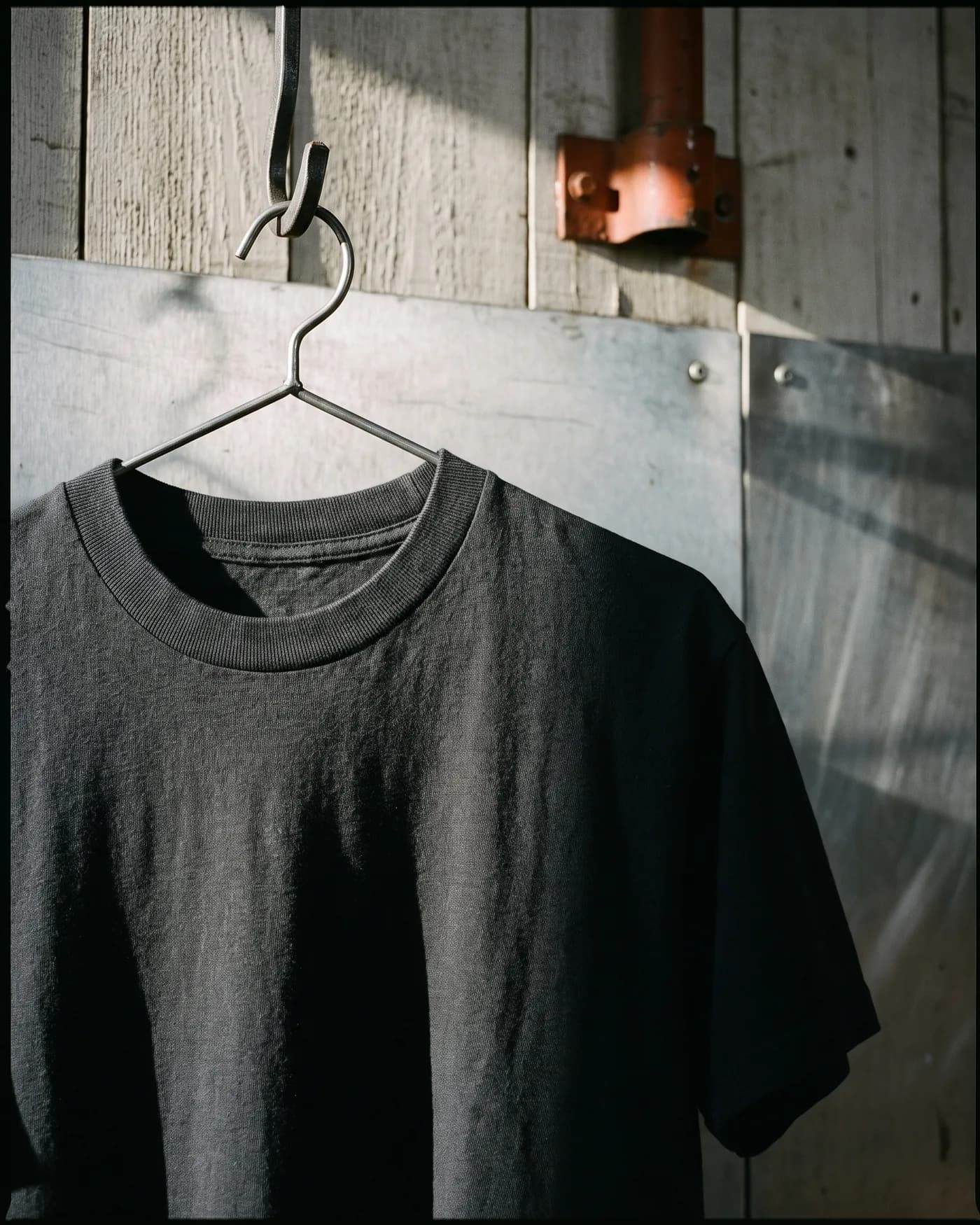 A heavyweight Steelwood tee hanging on a steel hook against weathered workshop timber